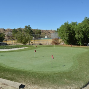 Artificial putting green with red flag pins and multiple turf speed zones installed at a desert valley golf practice facility