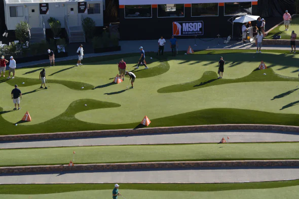 Professional artificial turf installation at a golf event venue, featuring contoured putting greens, multiple players practicing, and durable synthetic surfaces designed for high-traffic performance.