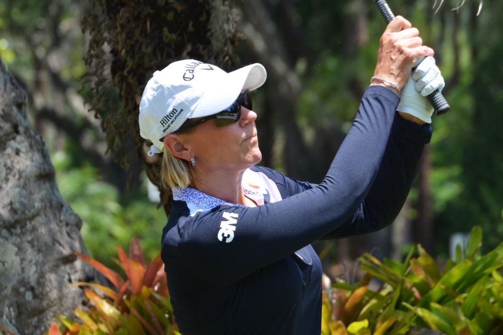Professional golfer Annika Sorenstam mid-swing on the course, wearing a white Hilton Grand Vacations cap and navy 3M long-sleeve shirt.