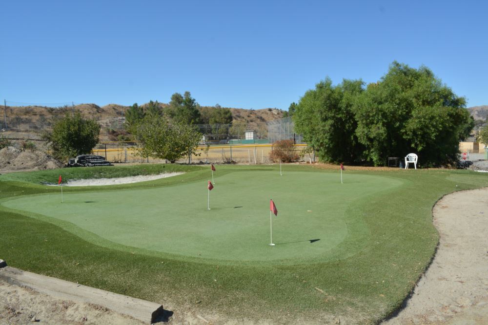 Artificial putting green with red flag pins and multiple turf speed zones installed at a desert valley golf practice facility