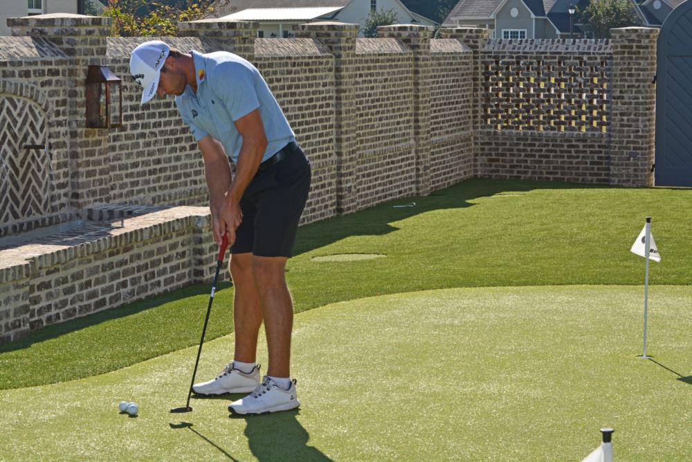 Sam Burns practicing on his custom Southwest Greens putting green and chipping area, featuring a brick courtyard wall and stone water feature
