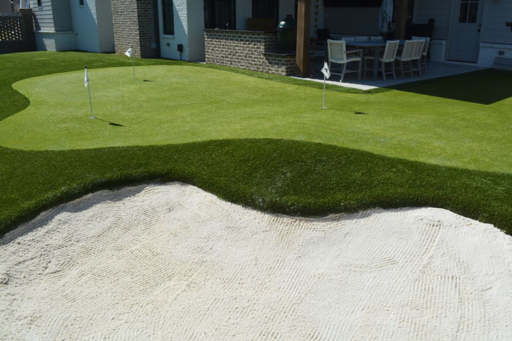 Close-up of a realistic sand bunker and putting green edge on Sam Burns&rsquo; Southwest Greens backyard golf course, with the home&rsquo;s covered patio in the background