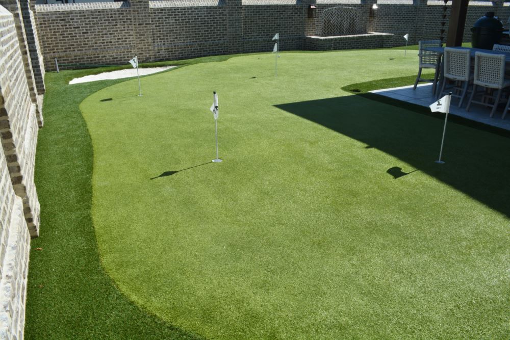 Overhead view of Sam Burns&rsquo; backyard putting green by Southwest Greens, showing multiple pin placements, a sand bunker, and an adjoining outdoor kitchen and bar